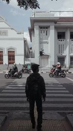 Rear view of man standing on street against building in city