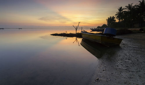 Boat moored on sea against sky at sunset