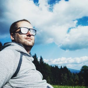 Low angle view of man sitting at park against cloudy sky