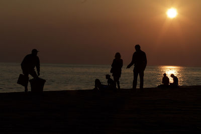 Silhouette people on beach against sky during sunset