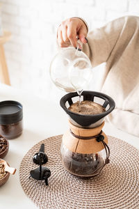 Young woman brewing coffee in chemex, pouring hot water into the filter