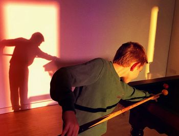 Boy playing pool against wall at home