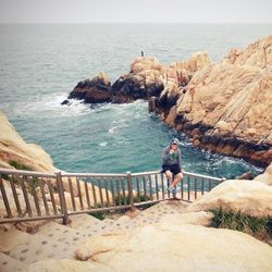 Man standing on rocks by sea against sky
