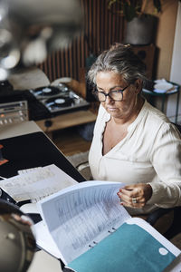 High angle view of businesswoman examining reports while sitting at desk in home office