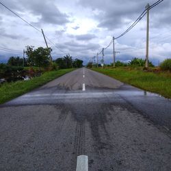 Road by electricity pylon against sky