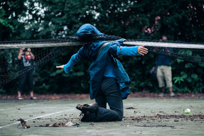 Rear view of boy in rain coats under a tennis net. 