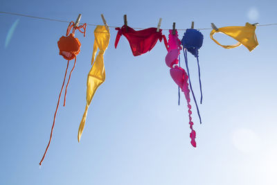 Low angle view of colorful female swimwear hanging against the blue sky 