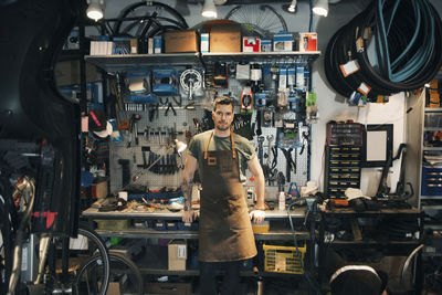 Portrait of confident mechanic leaning on workbench