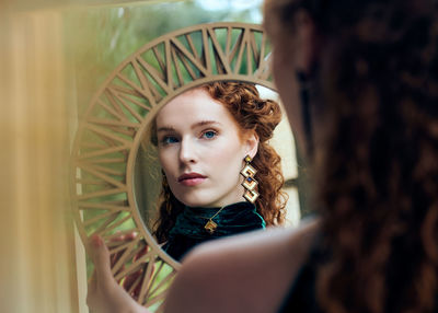 Portrait of beautiful young woman looking through mirror