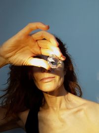 Woman holding crystal in front of face while standing against wall
