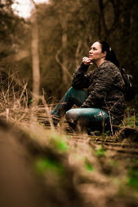 Young woman looking away while sitting on land in forest