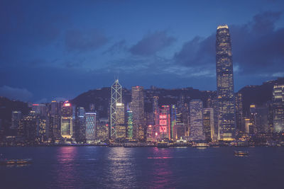 Illuminated city by sea against sky at night