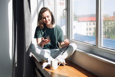 Portrait of young woman sitting on window