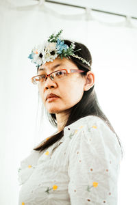 Portrait of young woman looking down while standing against white background