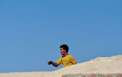 Full length of man using mobile phone against blue sky