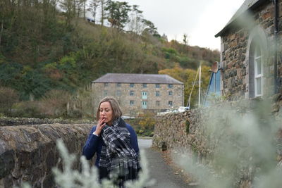 Mature woman smoking cigarette standing against building