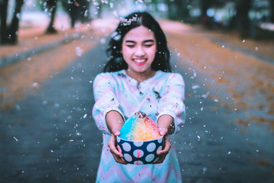 Smiling woman holding food in bowl on road