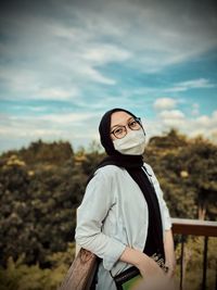 Portrait of woman wearing mask standing against sky