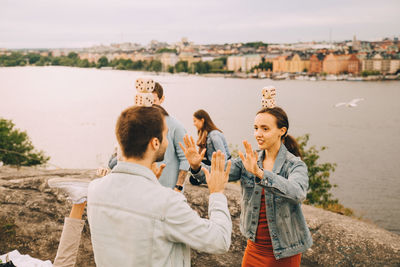 Male and female friends playing balancing games while standing on field by lake