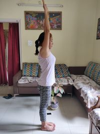 Side view full length of woman exercising in living room at home