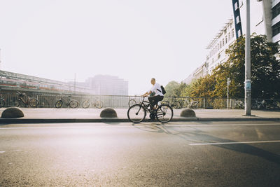 Full length of businessman with backpack riding bicycle on road in city against sky