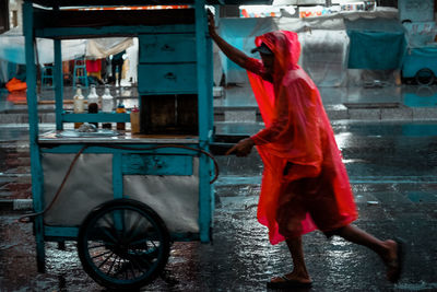 Man pushing cart on wet street during rainy season at night