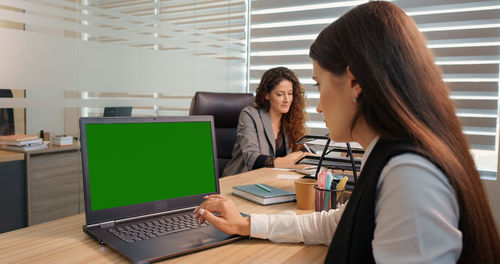 Businessman working on a laptop with green screen on background colleague discussing details. 