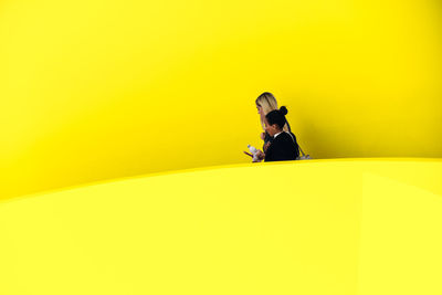 Full length of young woman against yellow background