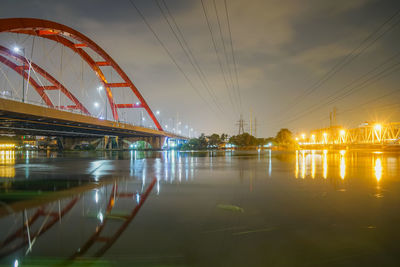 Illuminated ferris wheel by river against sky at night