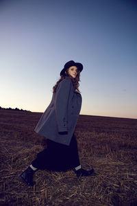 Woman in grey coat and black dress in field at sunset in autumn