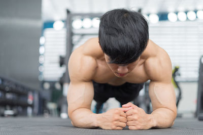 Shirtless man exercising in plank position at gym