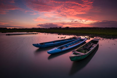 Rowboats moored in river against sky at sunset
