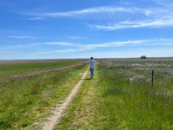 Rear view of woman walking on field against sky