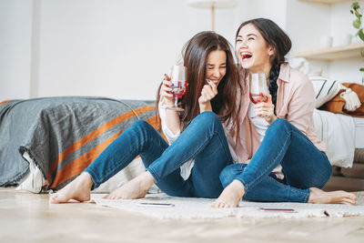 Cheerful female friends having drink while sitting at home