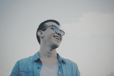 Low angle view of happy young man wearing eyeglasses against clear sky