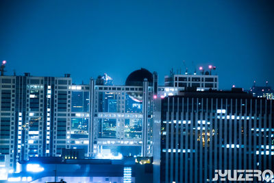 Illuminated buildings against clear blue sky at night