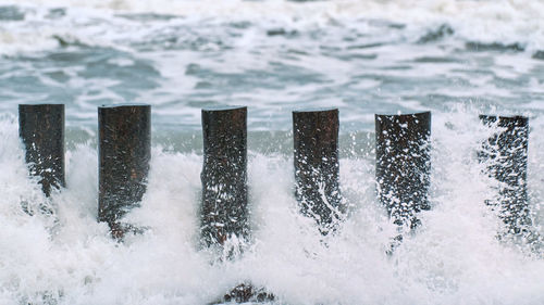 High wooden breakwaters in blue splashing sea waves, close up view. long poles, groynes. stormy sea