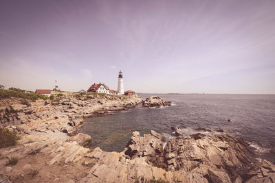 Lighthouse by sea and buildings against sky