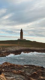 Lighthouse on beach by sea against sky