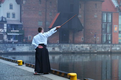 Man with stick standing by canal in city