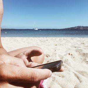 Close-up of hand holding sand at beach against clear sky