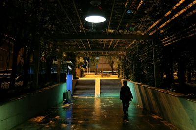 Silhouette man walking in illuminated wet walkway at night