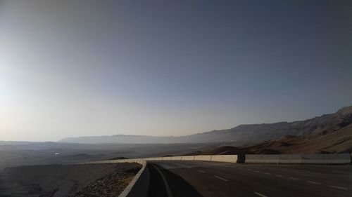 Road leading towards mountains against clear sky