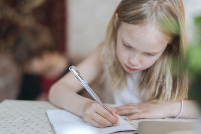 Blondie girl writing with pen while sitting on table