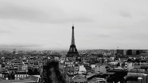 Communications tower in city against cloudy sky