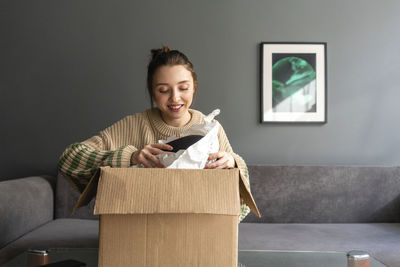 Smiling young woman sitting in box at home