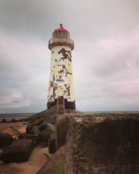 Lighthouse on shore against cloudy sky