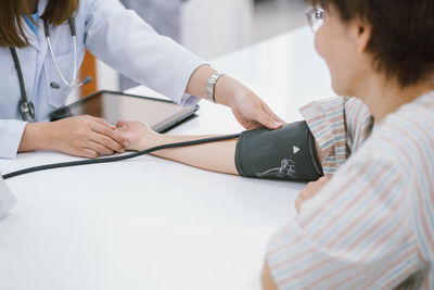 Midsection of doctor examining patient blood pressure with gauge by digital tablet on table