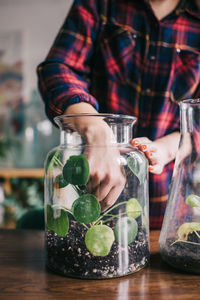 Midsection of woman planting plant in jar at home