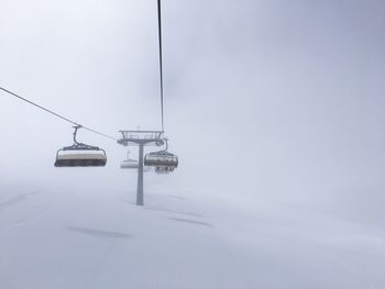 Snow covered overhead cable car against sky during winter